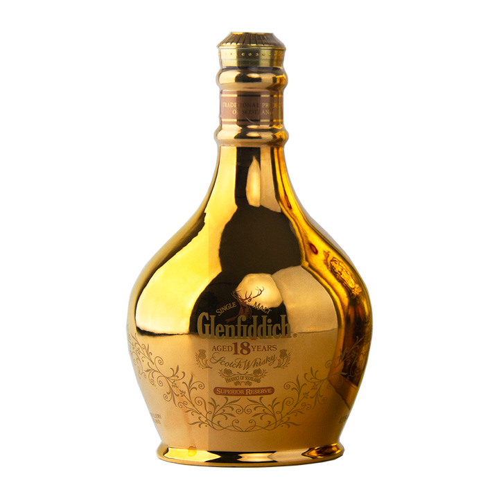 A gold, reflective ceramic decanter of Glenfiddich 18 Year Old Superior Reserve Single Malt Scotch Whisky features ornate detailing and a wide base tapering to a narrow neck, set against a plain white background.