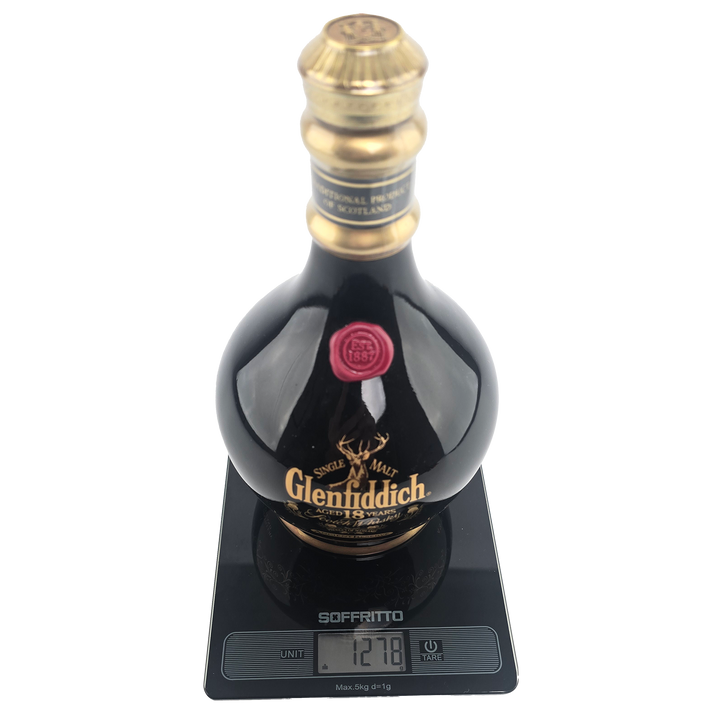 A bottle of Glenfiddich 18 Year Old Ancient Reserve Single Malt Scotch Whisky sits on a digital scale showing 1278g. With gold and red accents on its neck and label, this limited edition is a collectible decanter.