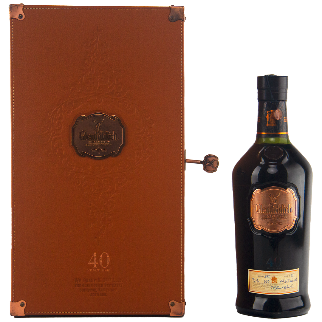 A Glenfiddich 40 Year Old Single Malt Scotch Whisky bottle in dark glass with a copper label is displayed beside an elegant brown leather case with embossed details and copper accents—an extraordinary limited edition release.