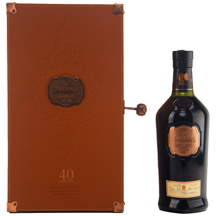 A Glenfiddich 40 Year Old Single Malt Scotch Whisky bottle in dark glass with a copper label is displayed beside an elegant brown leather case with embossed details and copper accents—an extraordinary limited edition release.