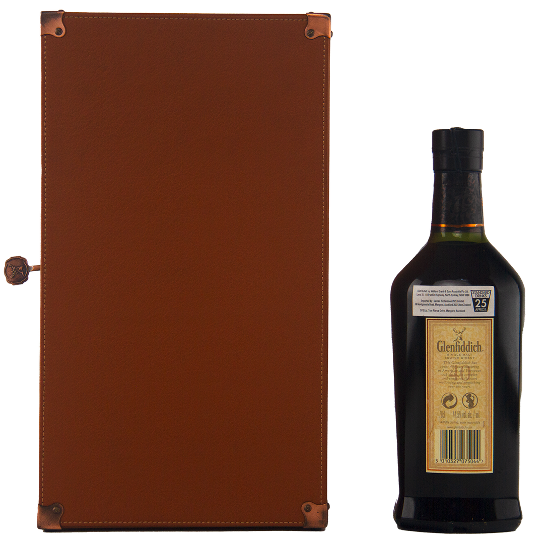 A bottle of Glenfiddich 40 Year Old Single Malt Scotch Whisky stands next to a closed brown leather case with metal corner protectors and a small clasp. The bottle’s label and cap are clearly visible.