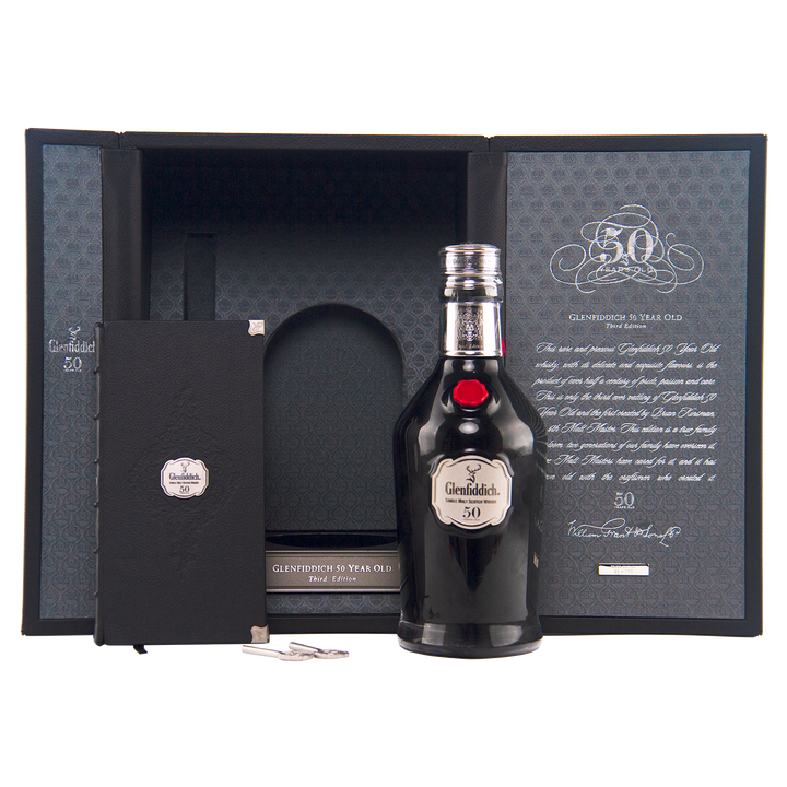 The Glenfiddich 50 Year Old Single Malt Scotch Whisky (Third Edition) is presented before an open display case, alongside a booklet, silver key, and certificate celebrating its extraordinary age and distinguished heritage.