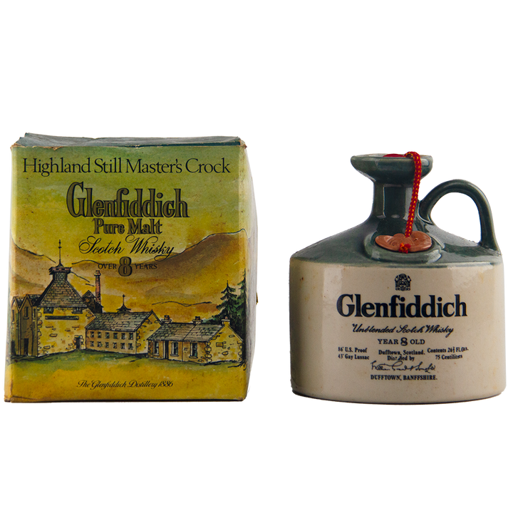 A Glenfiddich 8 Year Old Still Master’s Crock Decanter 1970 Single Malt Scotch Whisky, with handle and red seal, stands beside its illustrated “Highland Still Master’s Crock” box—a true collectible for whisky enthusiasts.