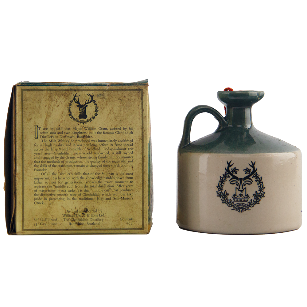 The Glenfiddich 8 Year Old Still Master’s Crock Decanter 1970, a collectible single malt whisky with green top, handle, and stag emblem, stands beside its original box showcasing matching text and logo.