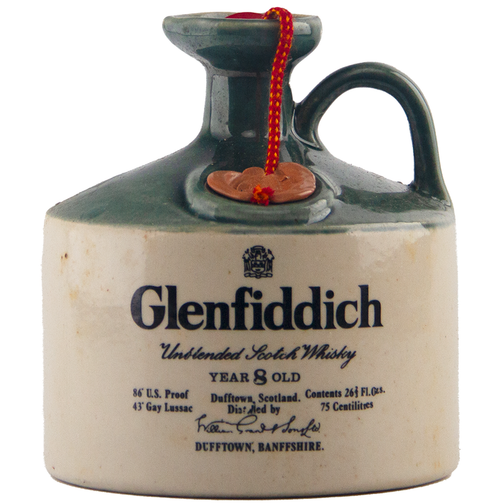 A collectible, the Glenfiddich 8 Year Old Still Master’s Crock Decanter 1970 Single Malt Scotch Whisky features a ceramic jug with a green neck, handle, red cord, and label highlighting its single malt Dufftown origins.