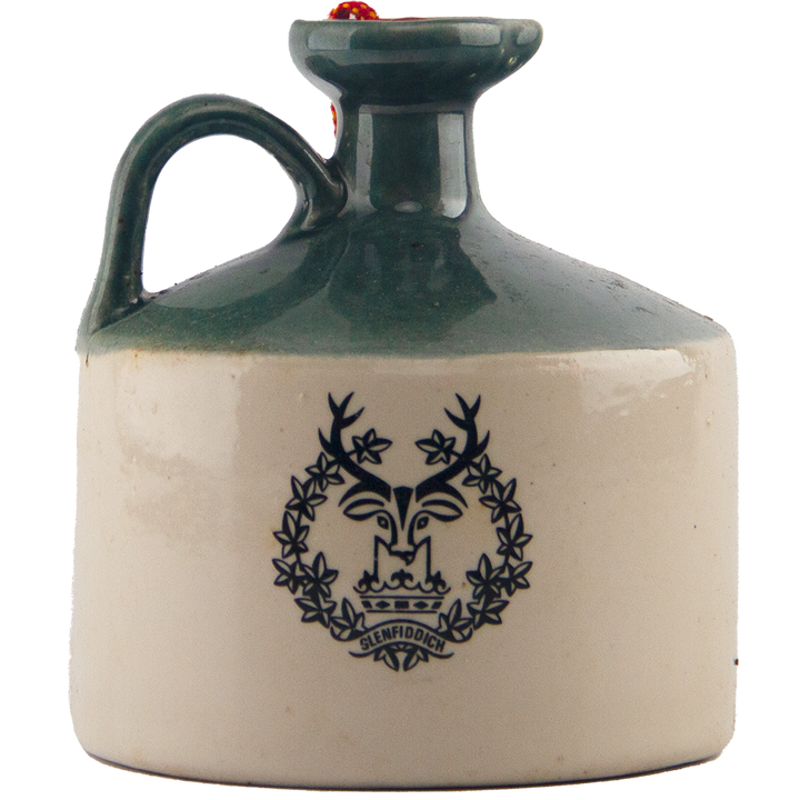A collectible Glenfiddich 8 Year Old Still Master’s Crock Decanter from 1970, this ceramic jug with green handle and rim features a black stag head logo, wreath, and Glenfiddich branding—ideal as a single malt Scotch whisky decanter.