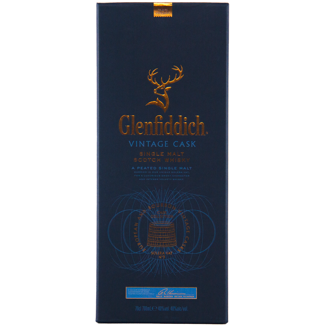 The dark blue Glenfiddich Vintage Cask Single Malt Scotch Whisky box features gold embossed text, a stag logo, and detailed designs, emphasizing its status as a peated single malt scotch exclusive to travel retail.