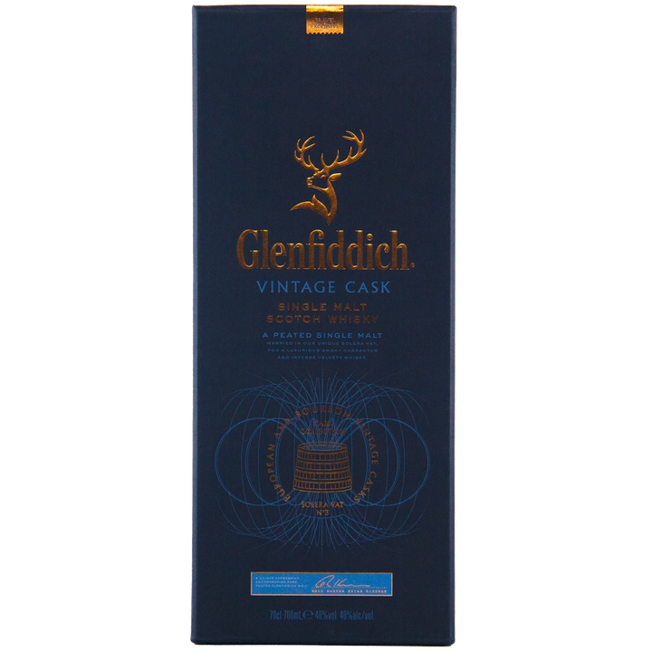 The dark blue Glenfiddich Vintage Cask Single Malt Scotch Whisky box features gold embossed text, a stag logo, and detailed designs, emphasizing its status as a peated single malt scotch exclusive to travel retail.