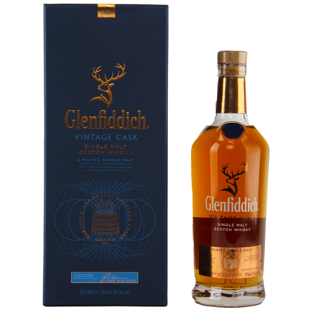 A bottle of Glenfiddich Vintage Cask Single Malt Scotch Whisky stands beside its blue and gold box adorned with a gold stag logo—this travel retail exclusive is an ideal choice for collectors.