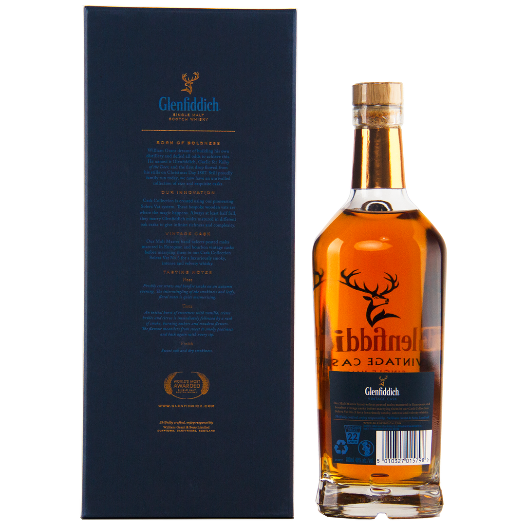 A bottle of Glenfiddich Vintage Cask Single Malt Scotch Whisky stands next to its dark blue box, both adorned with gold and white text and the iconic stag logo. This travel retail exclusive features a rich amber color.