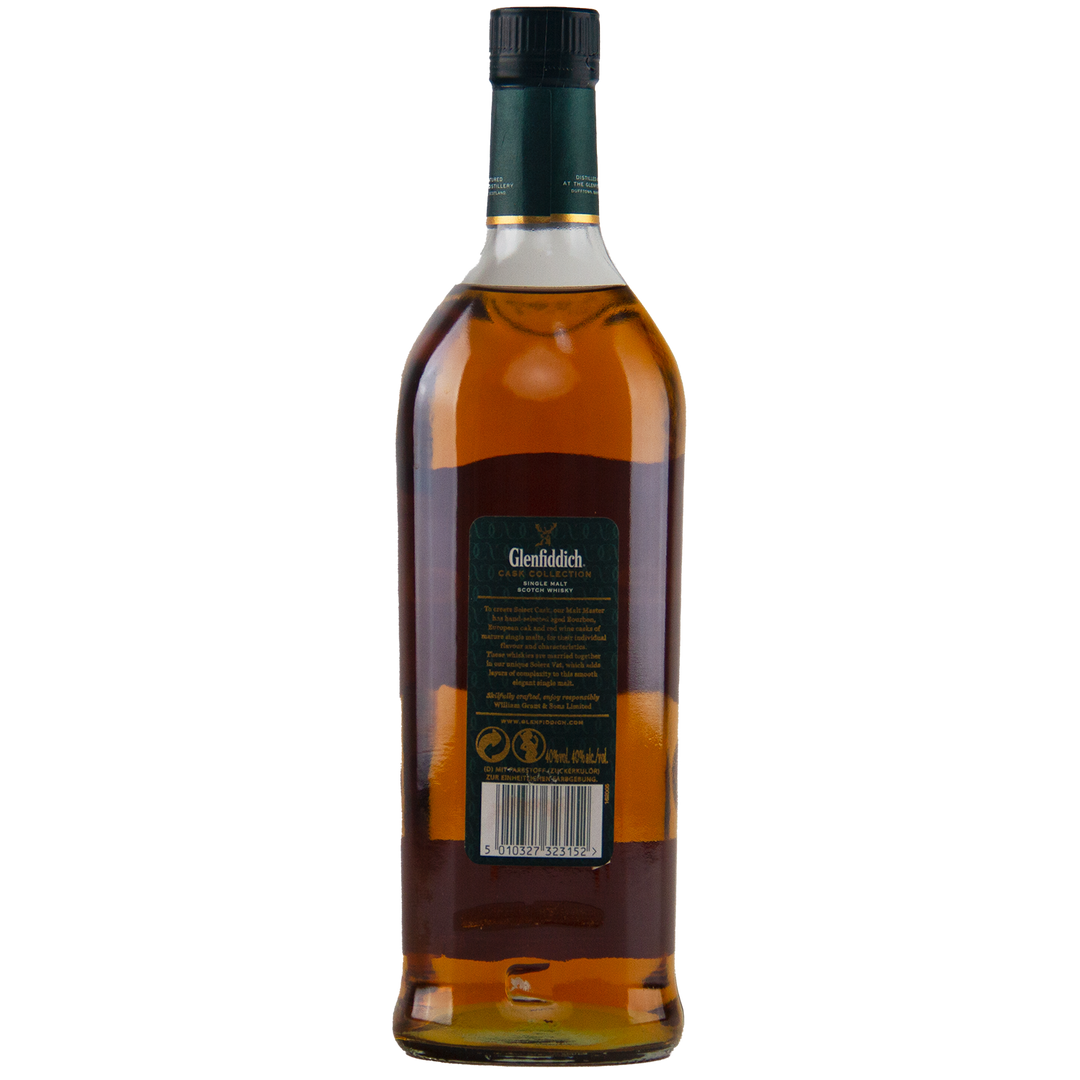 A bottle of Glenfiddich Select Cask Single Malt Scotch Whisky is shown from the back, displaying a green label with product details and barcode, sealed with a dark green cap. The amber whisky shines through the clear glass.