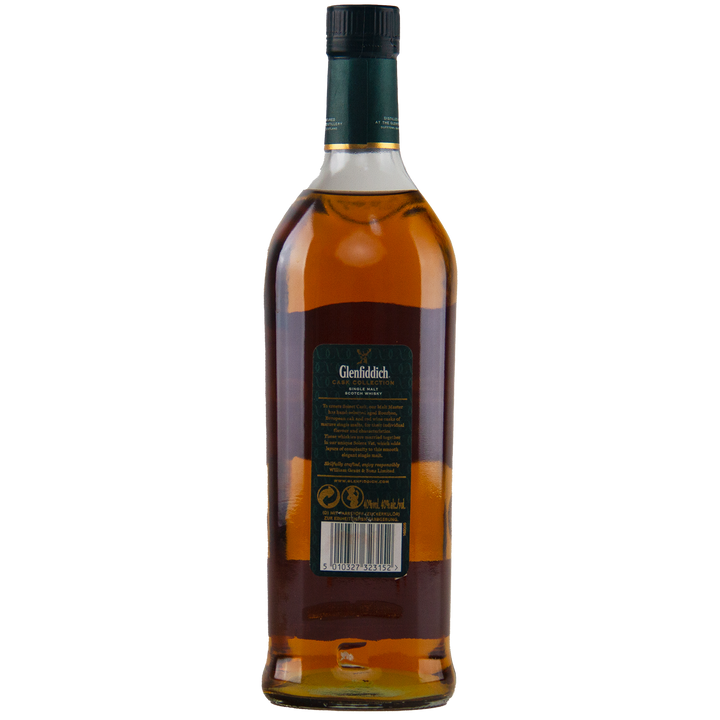 A bottle of Glenfiddich Select Cask Single Malt Scotch Whisky is shown from the back, displaying a green label with product details and barcode, sealed with a dark green cap. The amber whisky shines through the clear glass.