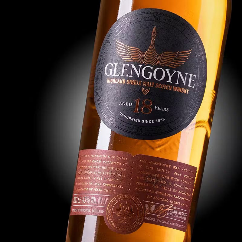 A close-up of the Glengoyne 18 Year Old Single Malt Whisky bottle highlights its black and copper label with intricate text and logo, set against amber whisky—a nod to its sherry cask maturation.