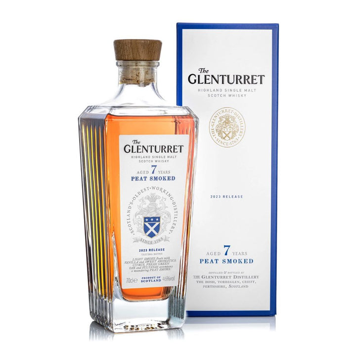 A bottle of Glenturret 7 Year Old Peat Smoked Single Malt Scotch Whisky stands before its blue and white box, amber liquid shining beneath the cork. Both label and box feature the brand's crest.