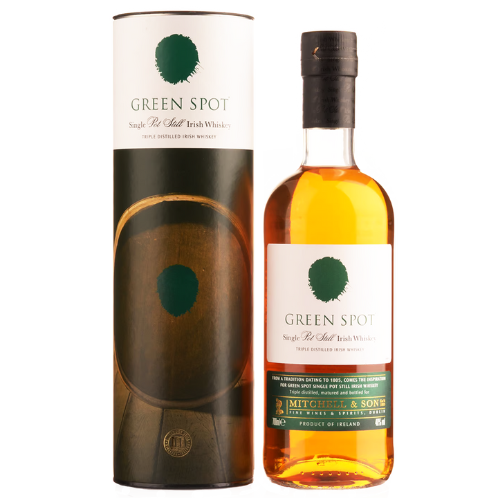 A bottle of Green Spot Single Pot Still Irish Whiskey stands next to its cylindrical packaging, both featuring white labels with a green spot logo and gold and green accents. The bottle contains golden amber whiskey.