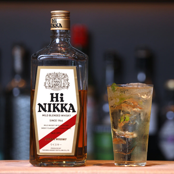 A bottle of Nikka Hi Nikka Blended Japanese Whisky sits on a bar counter beside a tall cocktail glass with ice and mint, with blurred bottles in the background.