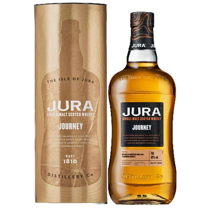 A bottle of Jura Journey Single Malt Scotch Whisky stands beside its matching gold cylindrical box, both with black and gold accents and branding details, emphasizing maturation in American white oak ex-bourbon barrels.