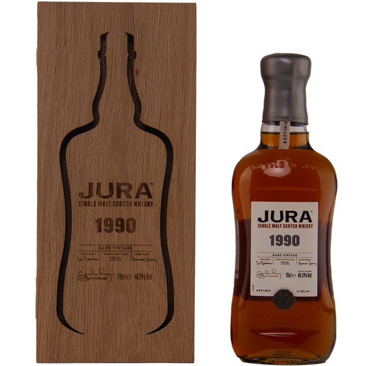A bottle of Jura 1990 30 Year Old Single Malt Whisky stands beside a wooden box with a bottle-shaped cutout and engraved text. The bottle has a dark wax seal and a white label with black and gold accents—a true collectible Scotch.