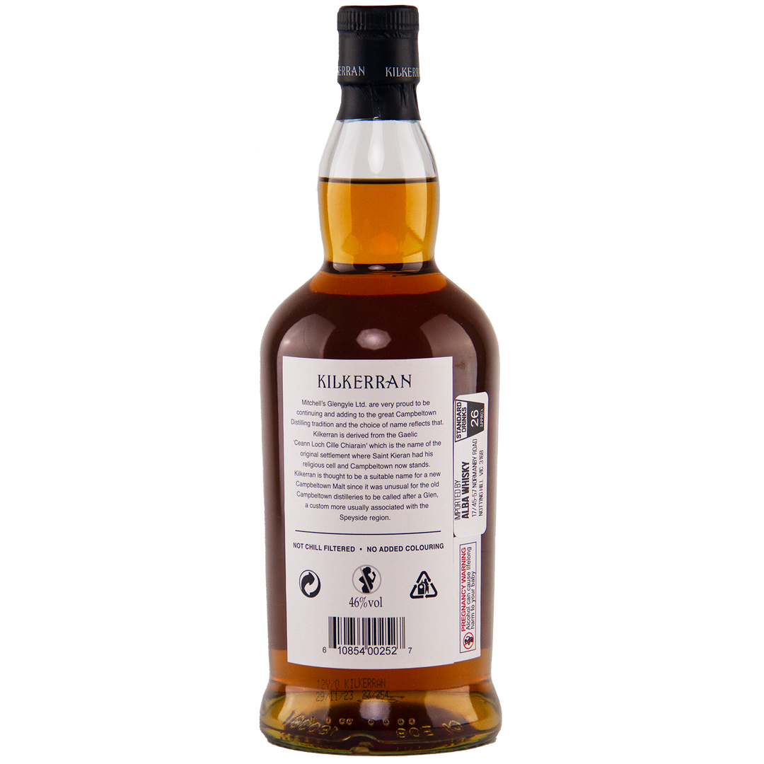 A bottle of Kilkerran 12 Year Old Single Malt Scotch Whisky is shown from the back, featuring a white label with text, barcodes, and symbols. The amber whisky and black cap display distinctive Glengyle Distillery branding.