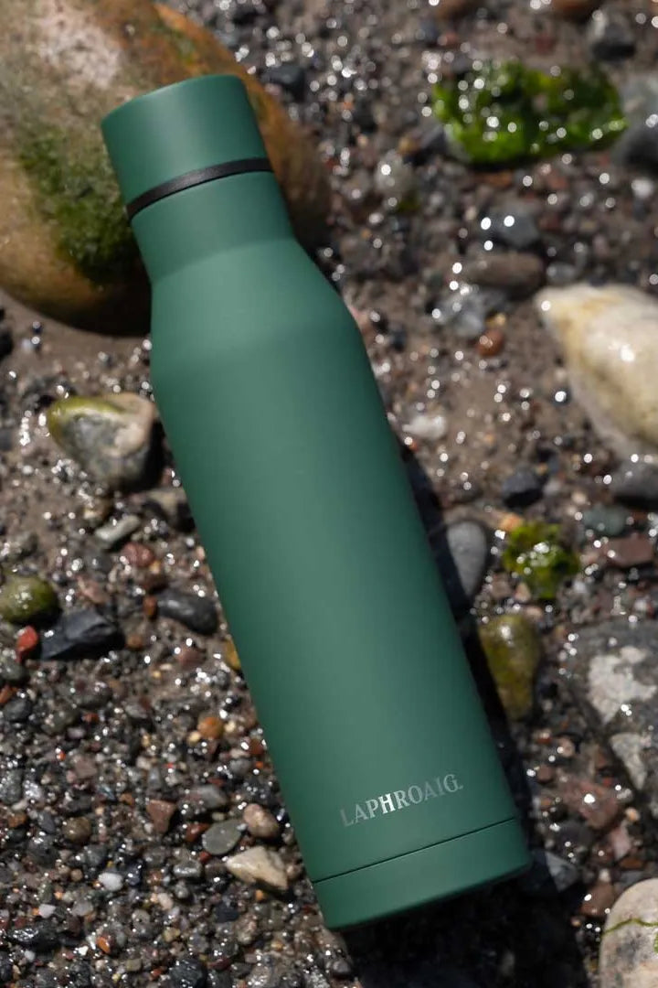 Green water bottle with 'LAPHROAIG' branding on a pebbly surface