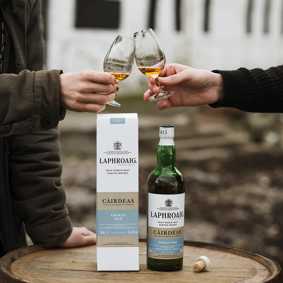 Two people toasting with Laphroaig Cairdeas whisky on a wooden barrel.