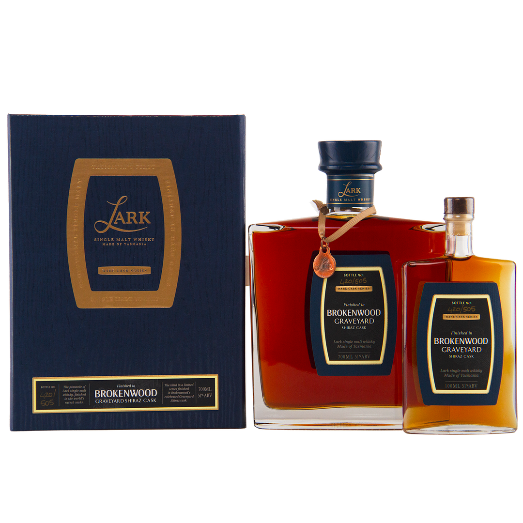 Two bottles of Lark Brokenwood Graveyard Shiraz Rare Cask Single Malt Whisky, one large and one small, with square bodies and black-gold labels, are displayed beside a dark blue and gold gift box bearing the product name.
