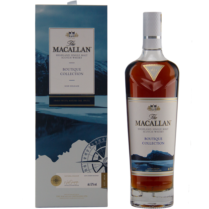 A bottle of The Macallan Boutique Collection 2019 Release Single Malt Whisky stands by its blue and white box, featuring mountain and lake artwork that emphasizes its travel retail exclusivity.