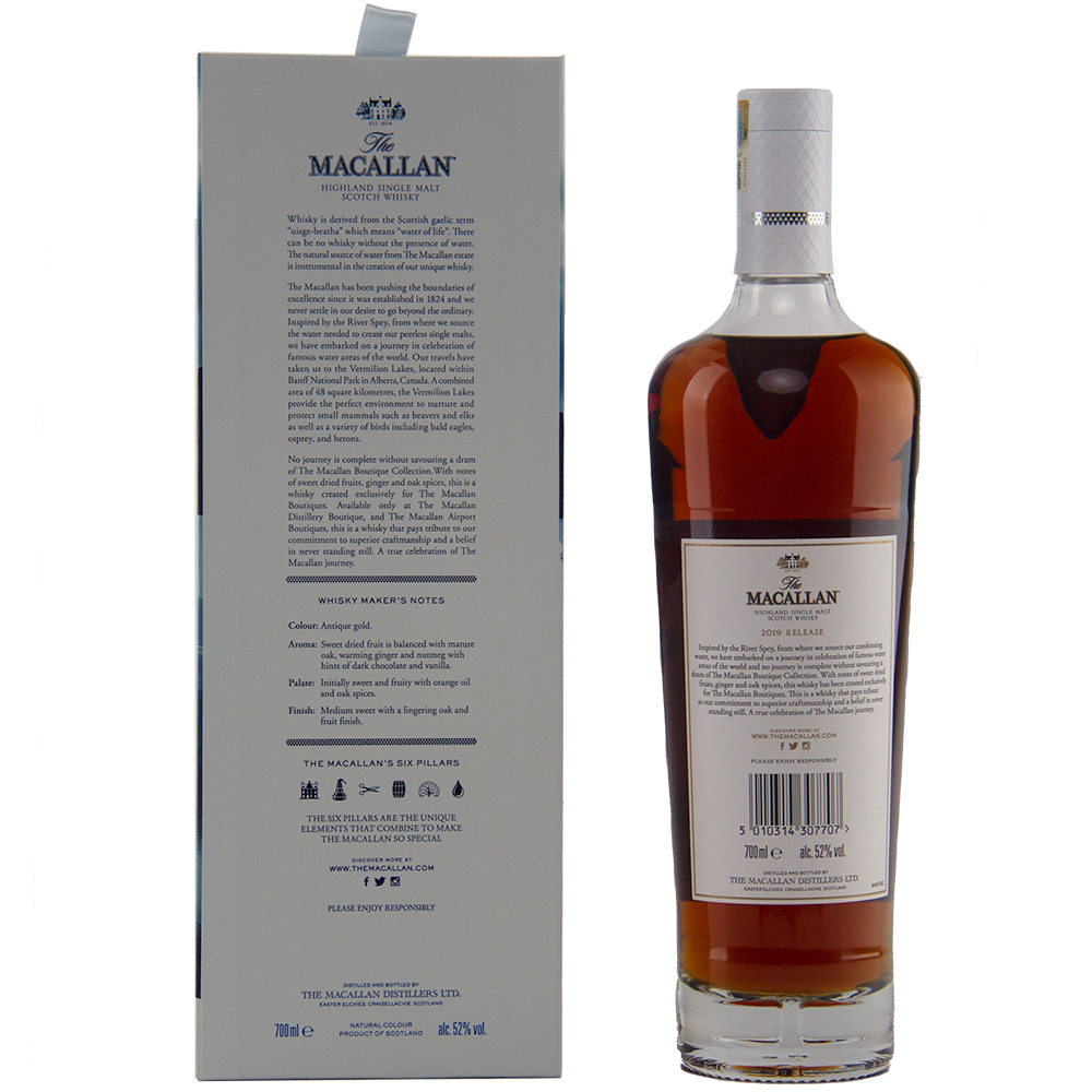A bottle of The Macallan Boutique Collection 2019 Release Single Malt Whisky stands beside its grey box packaging. The dark amber whisky is presented in a white label with gold and black accents, highlighting its travel retail exclusivity.