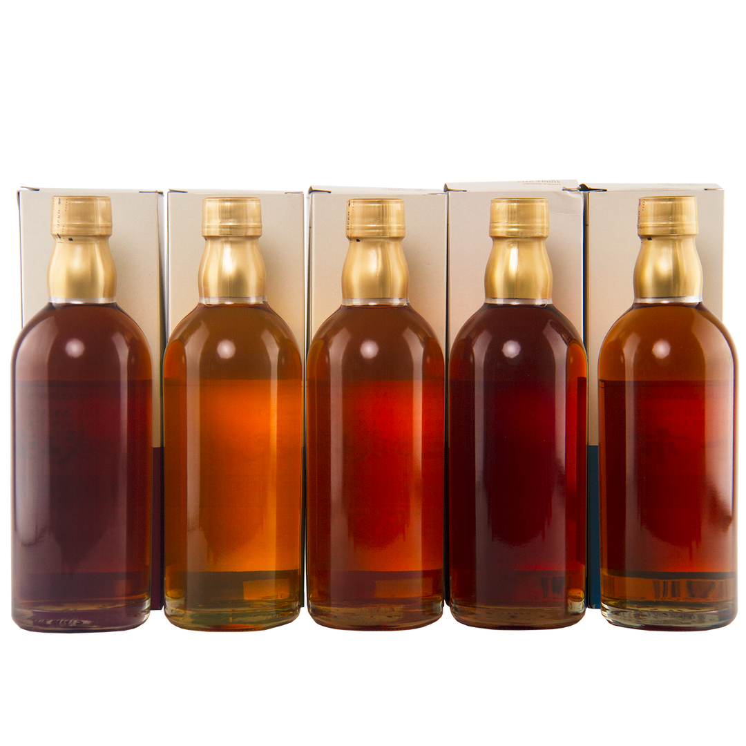 Five glass bottles with golden caps, each holding unique shades of amber whisky, stand before white boxes—a striking presentation of the Nikka Whisky Limited 5 Bottle Collection featuring Japanese single malt limited editions.