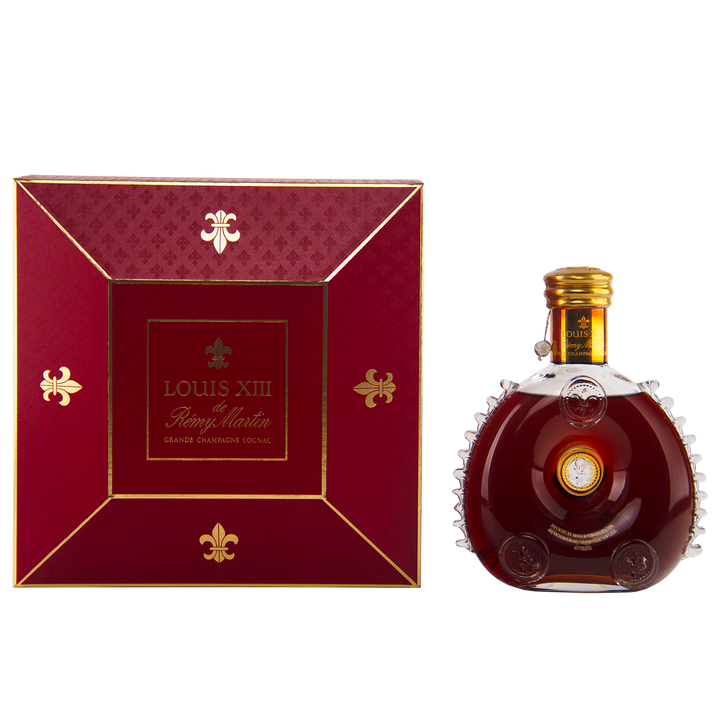 A 700mL bottle of Rémy Martin Louis XIII 1980s Edition Cognac Grande Champagne sits in a Baccarat crystal decanter beside its elegant red and gold box, both featuring the iconic branding.