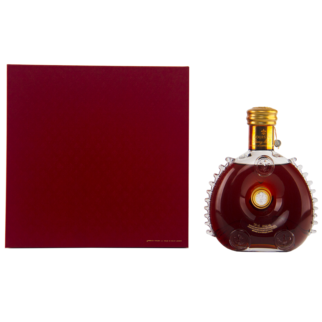 A round Baccarat crystal decanter of Rémy Martin Louis XIII 1980s Edition Cognac Grande Champagne 700mL with a gold cap stands next to a large, square dark red box on a white background.