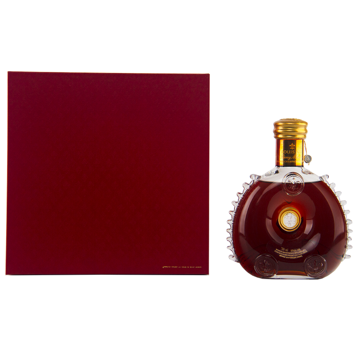 A round Baccarat crystal decanter of Rémy Martin Louis XIII 1980s Edition Cognac Grande Champagne 700mL with a gold cap stands next to a large, square dark red box on a white background.