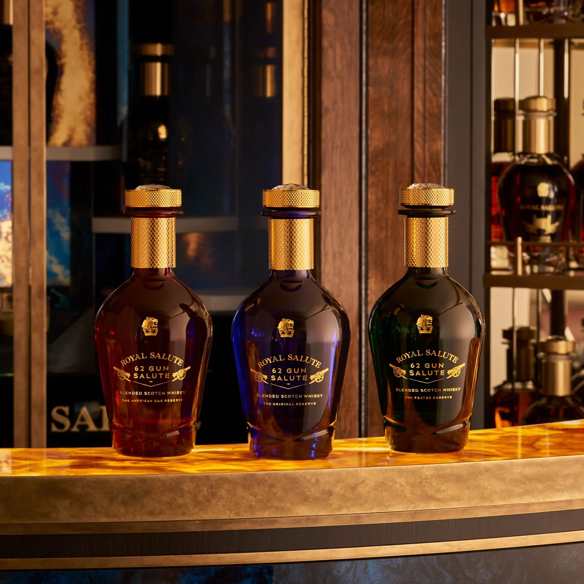 Three bottles of Royal Salute 42 Gun Salute whisky on a bar counter with a blurred bar background.
