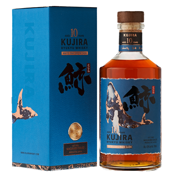 A bottle of Kujira Ryukyu 10 Year Old Japanese Whisky stands next to its blue box, both decorated with Japanese calligraphy and a whale illustration. The amber single grain whisky is finished in white oak virgin casks.