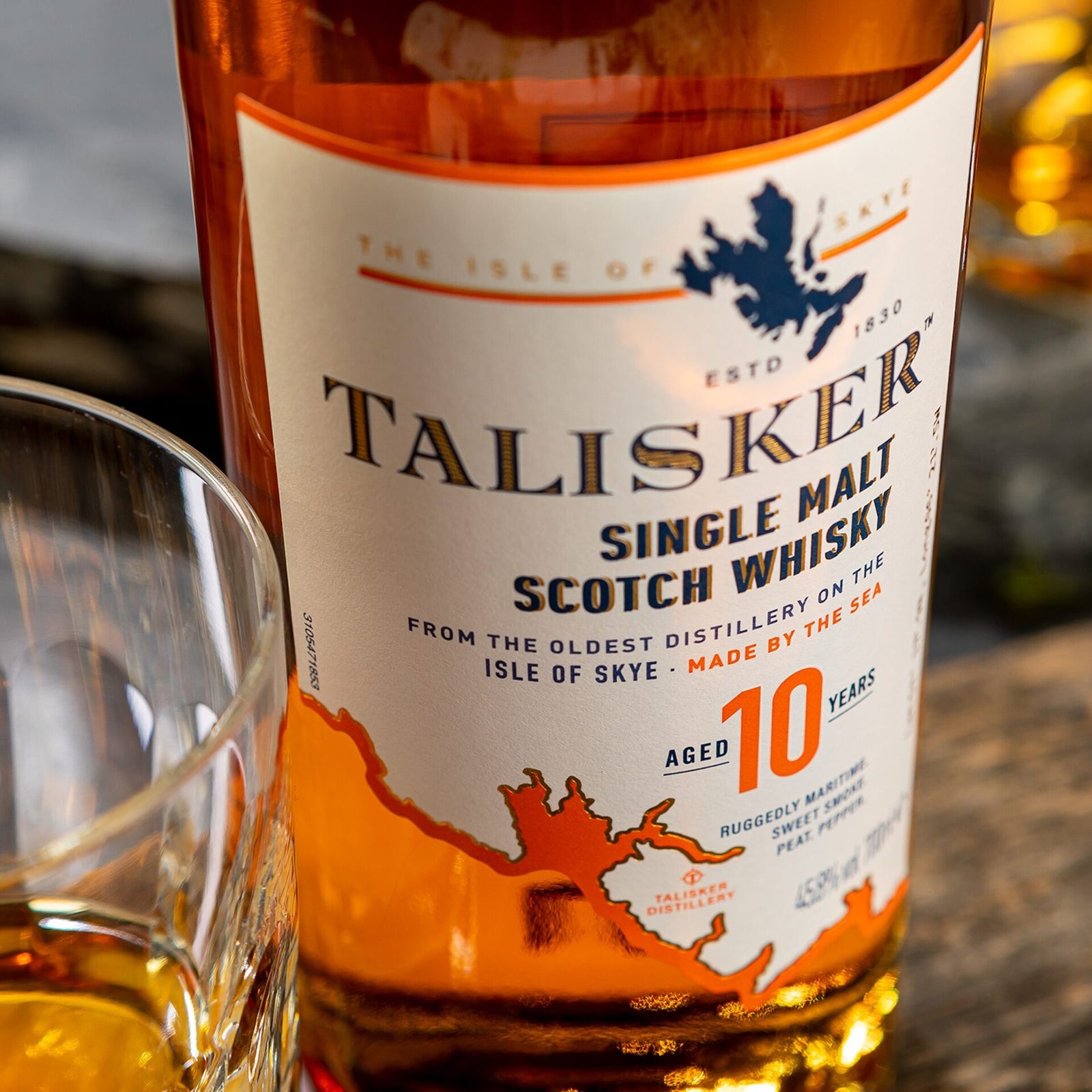 Close-up of a Talisker 10 Year Old Single Malt Scotch Whisky label, showcasing its peated origins from the Isle of Skye, with part of a whisky glass next to the bottle.