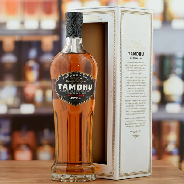 Tamdhu whisky bottle with packaging on a wooden surface, blurred bottles in the background