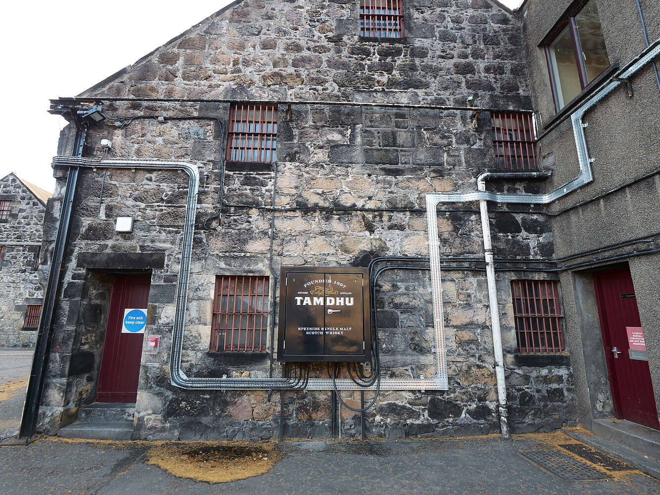 Grayscale image of a stone building with 'Tamdhu' sign on a street.