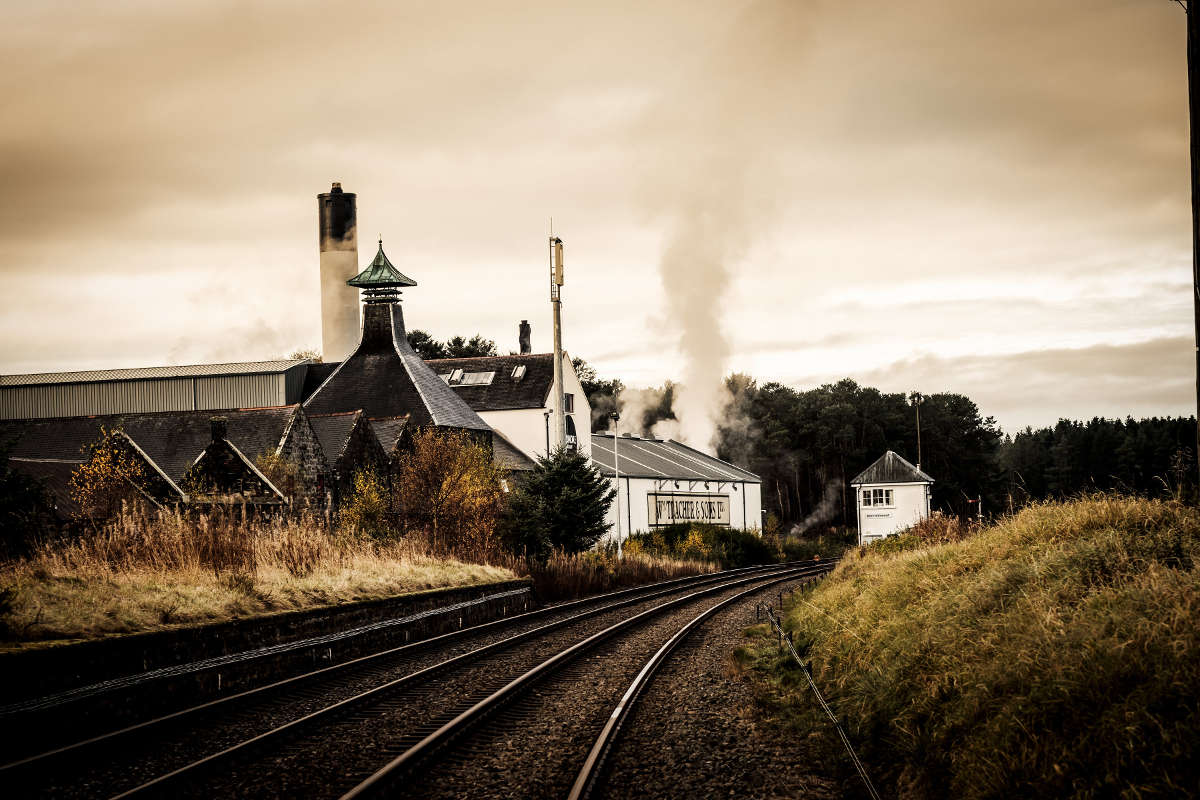 Factory or industrial building with smokestacks and train tracks in the foreground.