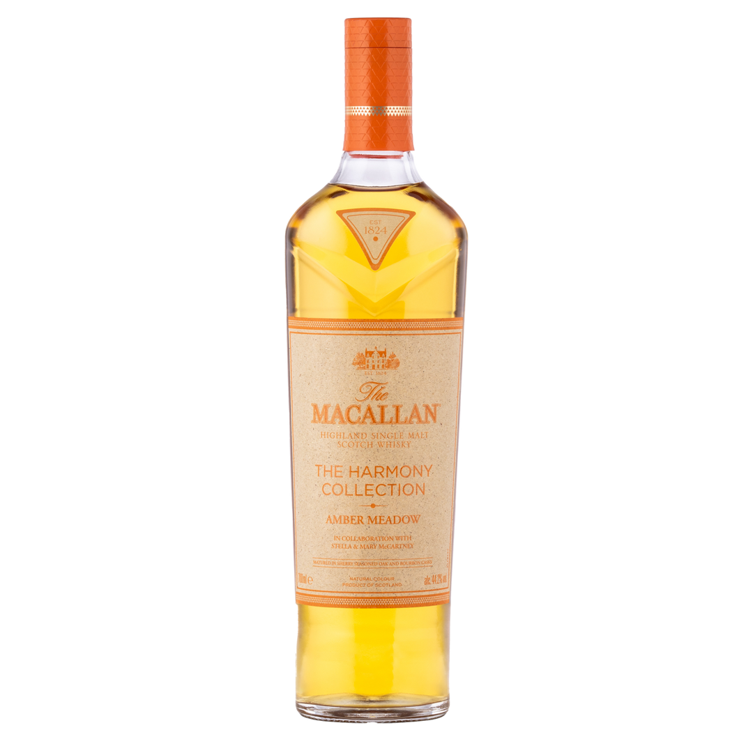 A bottle of The Macallan Harmony Collection Amber Meadow Single Malt Scotch Whisky with sustainable packaging, light amber liquid, and an orange cap and label on a plain white background.