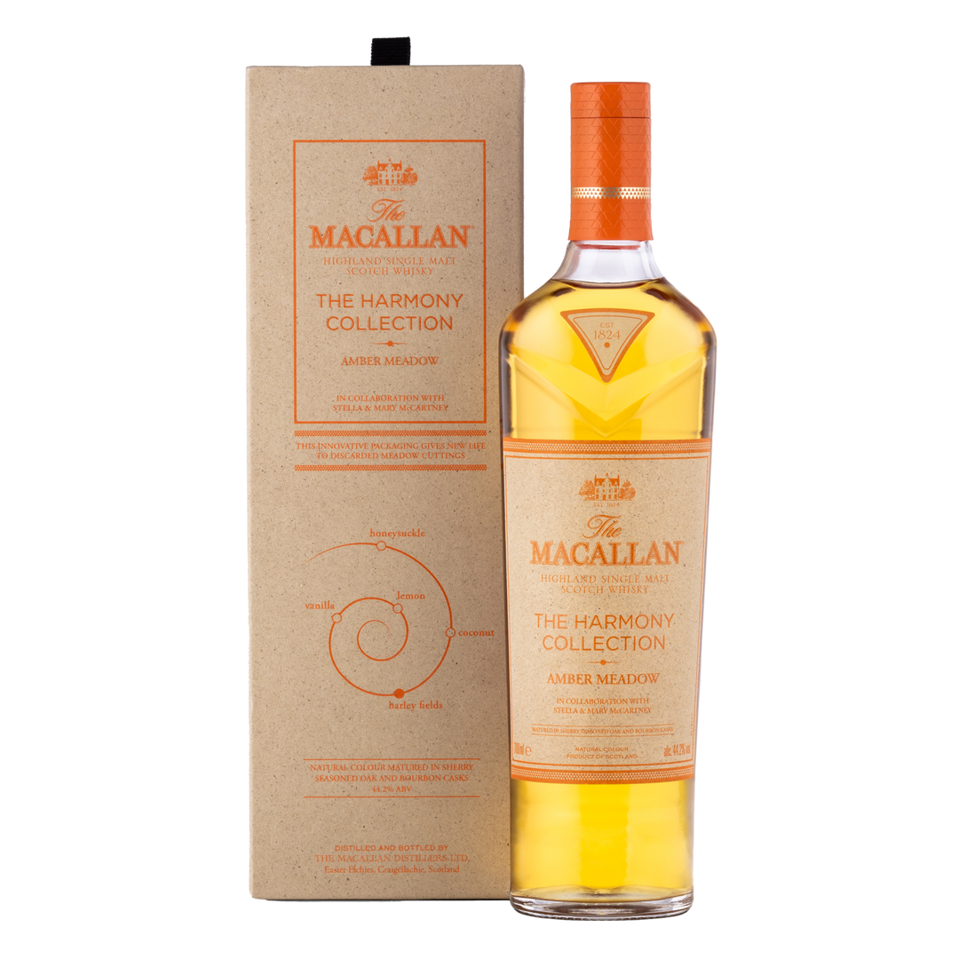 A bottle of The Macallan Harmony Collection Amber Meadow Single Malt Scotch Whisky stands beside its light brown box, both adorned with orange and gold accents and crafted from sustainable packaging.