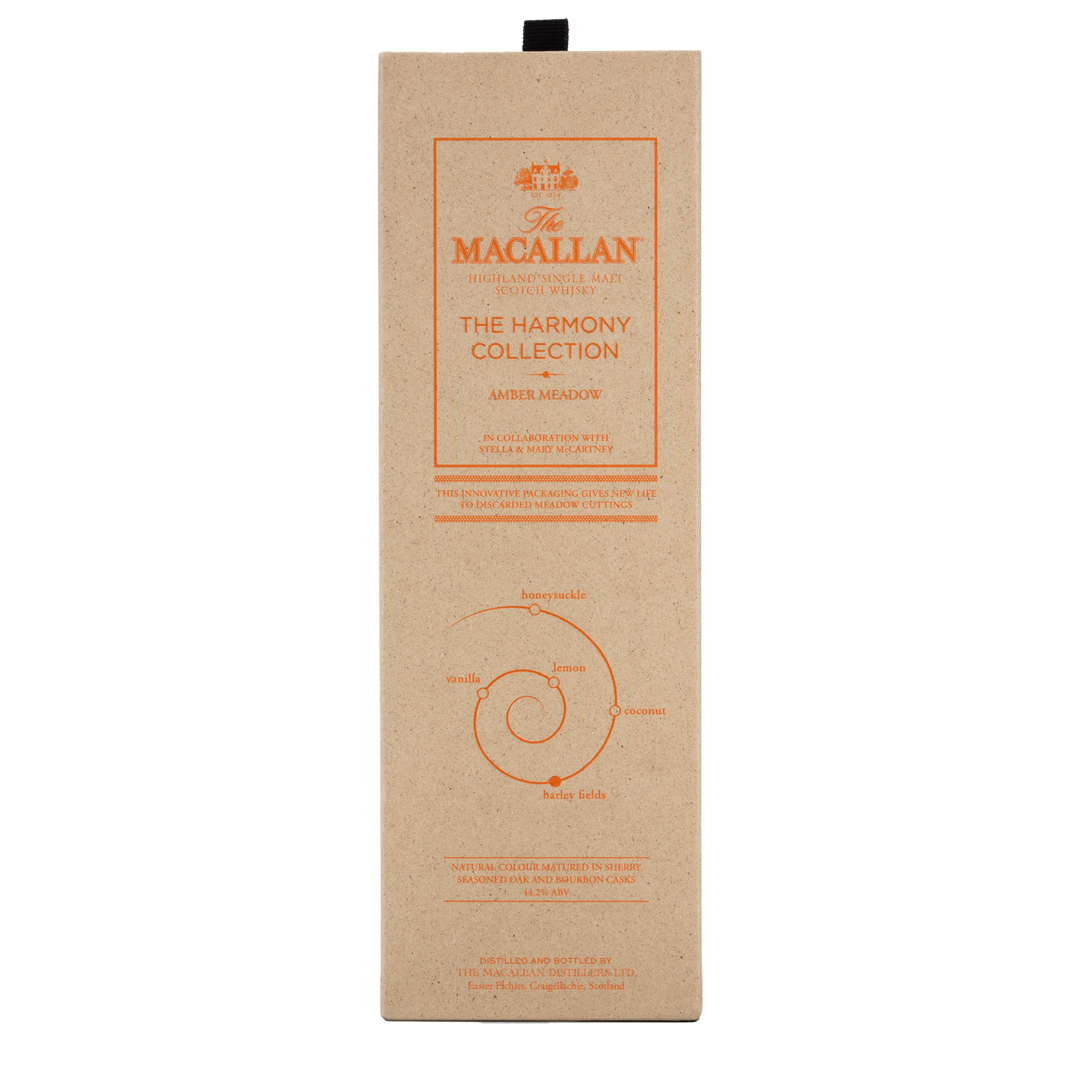 A beige rectangular box with orange text and graphics, labeled The Macallan Harmony Collection Amber Meadow Single Malt Scotch Whisky. This limited edition features a spiral design and highlights natural Scottish ingredients and sustainable packaging.
