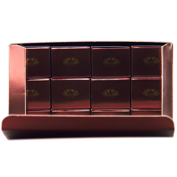 A box of twelve glossy, rectangular chocolates in a metallic tray—each embossed with gold logos—elegantly inspired by The Macallan 12 Year Old Sherry Oak Cask 12X50ml, with the lid partially open to reveal the luxurious treats inside.