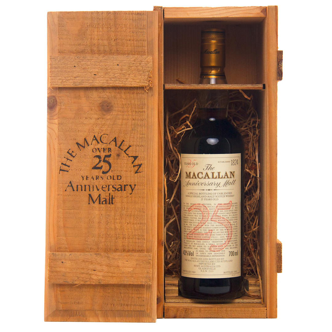 A bottle of The Macallan 1969 25 Year Old Anniversary Edition rests in a wooden presentation box with straw lining. The open lid reveals the whisky and branded text, emphasizing its prized sherry cask heritage.