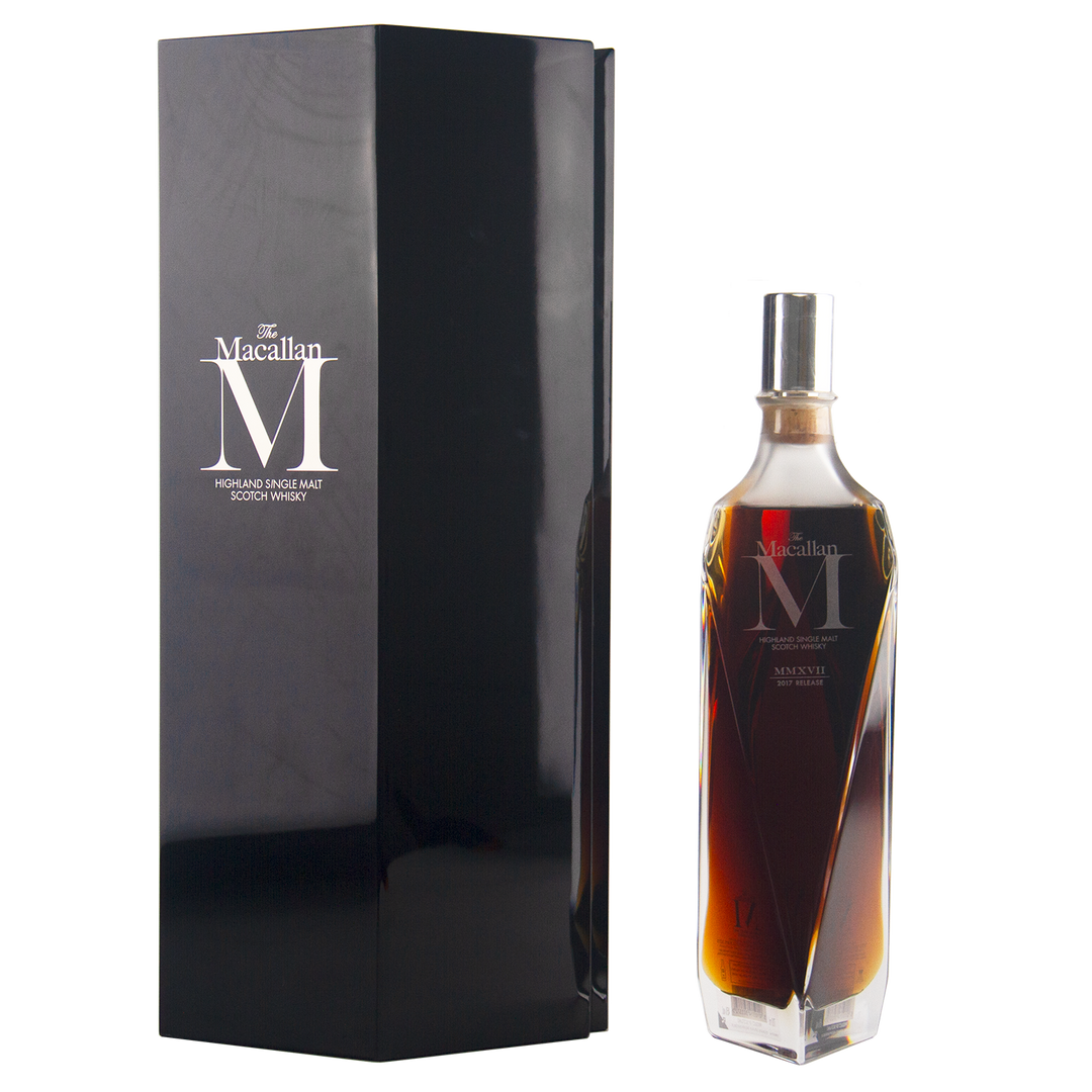 A sleek, angular bottle of The Macallan M (2017 First Release) Single Malt Scotch Whisky stands beside a tall black box, both with elegant silver branding—a tribute to sherry oak maturation.