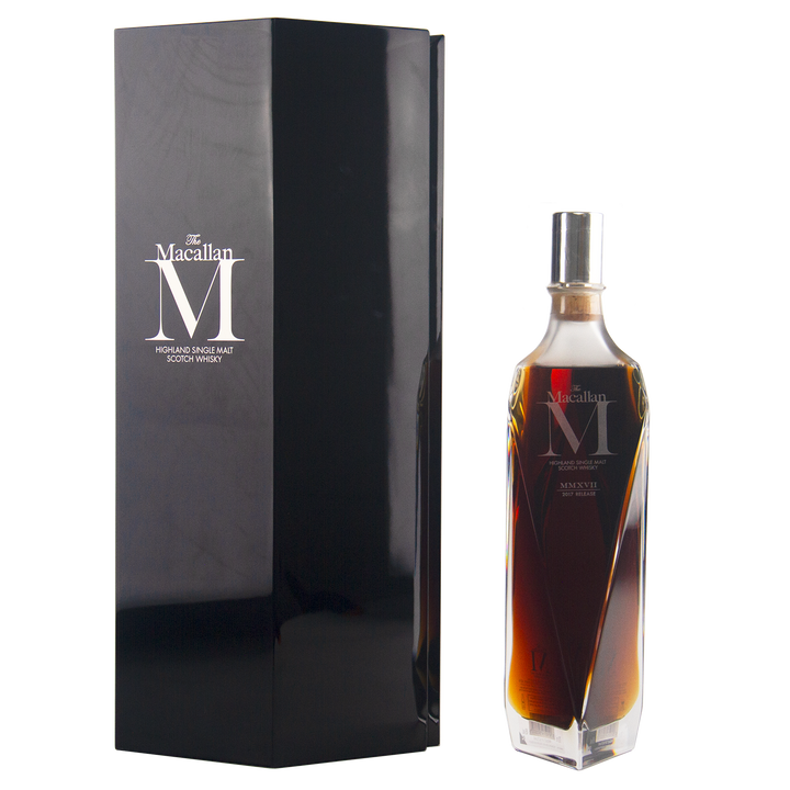 A sleek, angular bottle of The Macallan M (2017 First Release) Single Malt Scotch Whisky stands beside a tall black box, both with elegant silver branding—a tribute to sherry oak maturation.