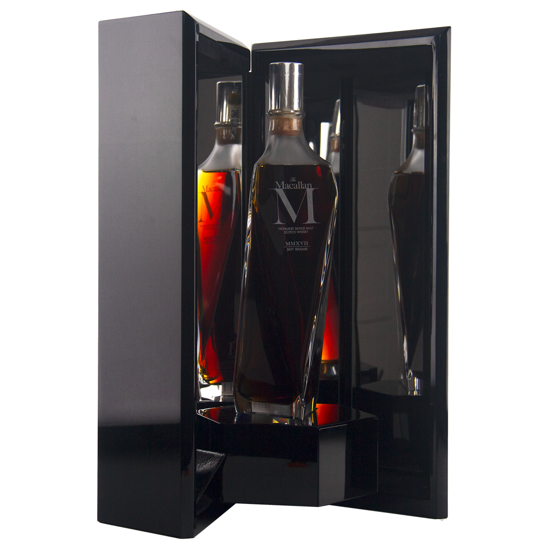 A dark, sleek display case reveals The Macallan M (2017 First Release) Single Malt Scotch Whisky, its clear angular bottle with a silver cap reflecting on glossy surfaces and showcasing its sherry oak maturation.