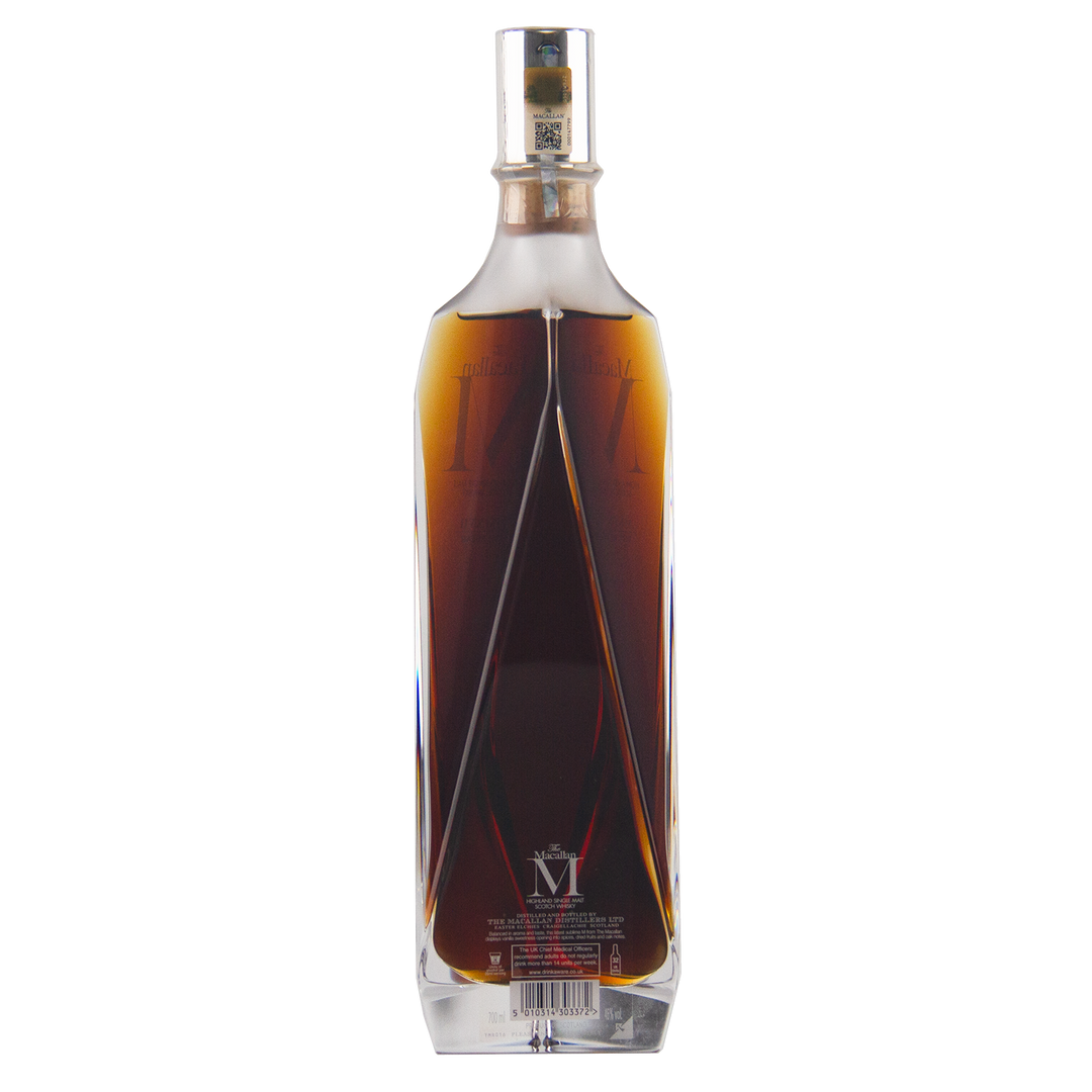 A bottle of The Macallan M (2017 First Release) Single Malt Scotch Whisky in a geometric clear crystal decanter with dark amber liquid, displayed against a white background and highlighting its rich sherry oak maturation.