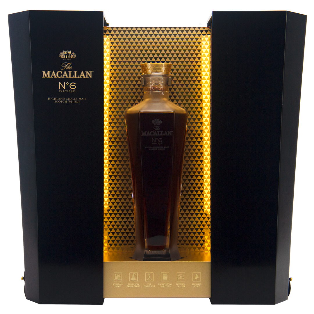 A bottle of The Macallan No 6 Single Malt Scotch Whisky rests in a hexagonal decanter within an elegant black and gold display box, featuring a honeycomb-patterned backdrop.