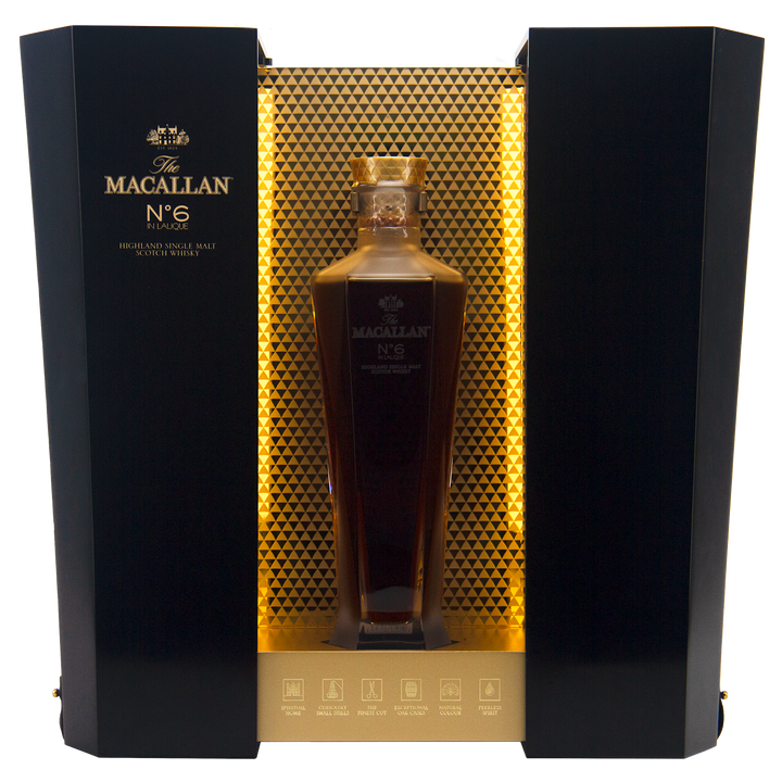 A bottle of The Macallan No 6 Single Malt Scotch Whisky rests in a hexagonal decanter within an elegant black and gold display box, featuring a honeycomb-patterned backdrop.