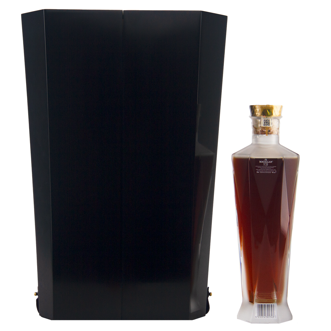 A tall black box stands beside an elegant, angular bottle of The Macallan No 6 Single Malt Scotch Whisky, filled with dark amber liquid and topped with a gold cap, both set against a plain white background.